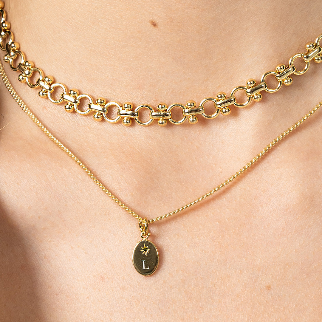 Two gold necklaces on a person's neck with one featuring an 'L' pendant.