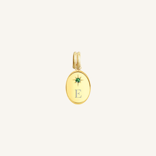 Gold pendant with a green gemstone and letter 'E' on a light beige background