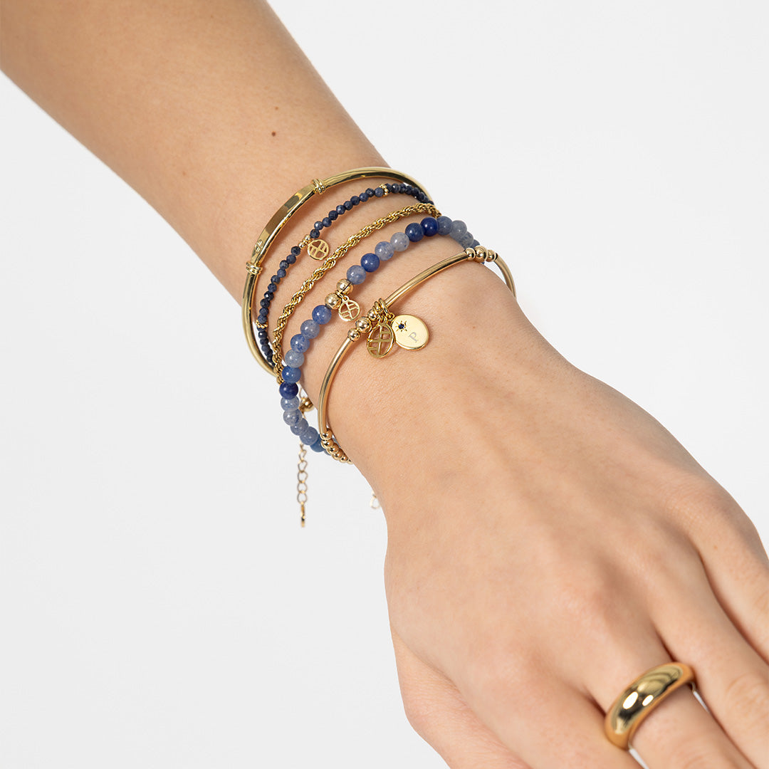 Hand wearing multiple gold and blue beaded bracelets on a light gray background