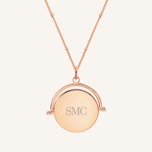 A rose-coloured pendant with the initials  engraved on it, featuring a spinning mechanism, on gold chain