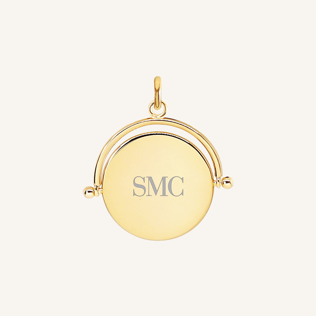 A gold-coloured pendant with the initials  engraved on it, featuring a spinning mechanism.