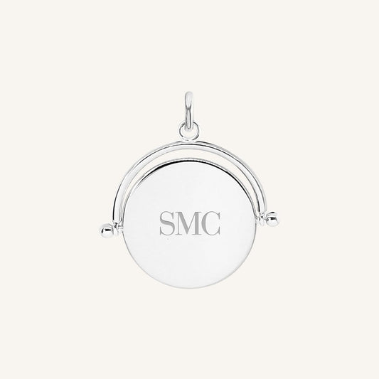 A silver-coloured pendant with the initials  engraved on it, featuring a spinning mechanism.