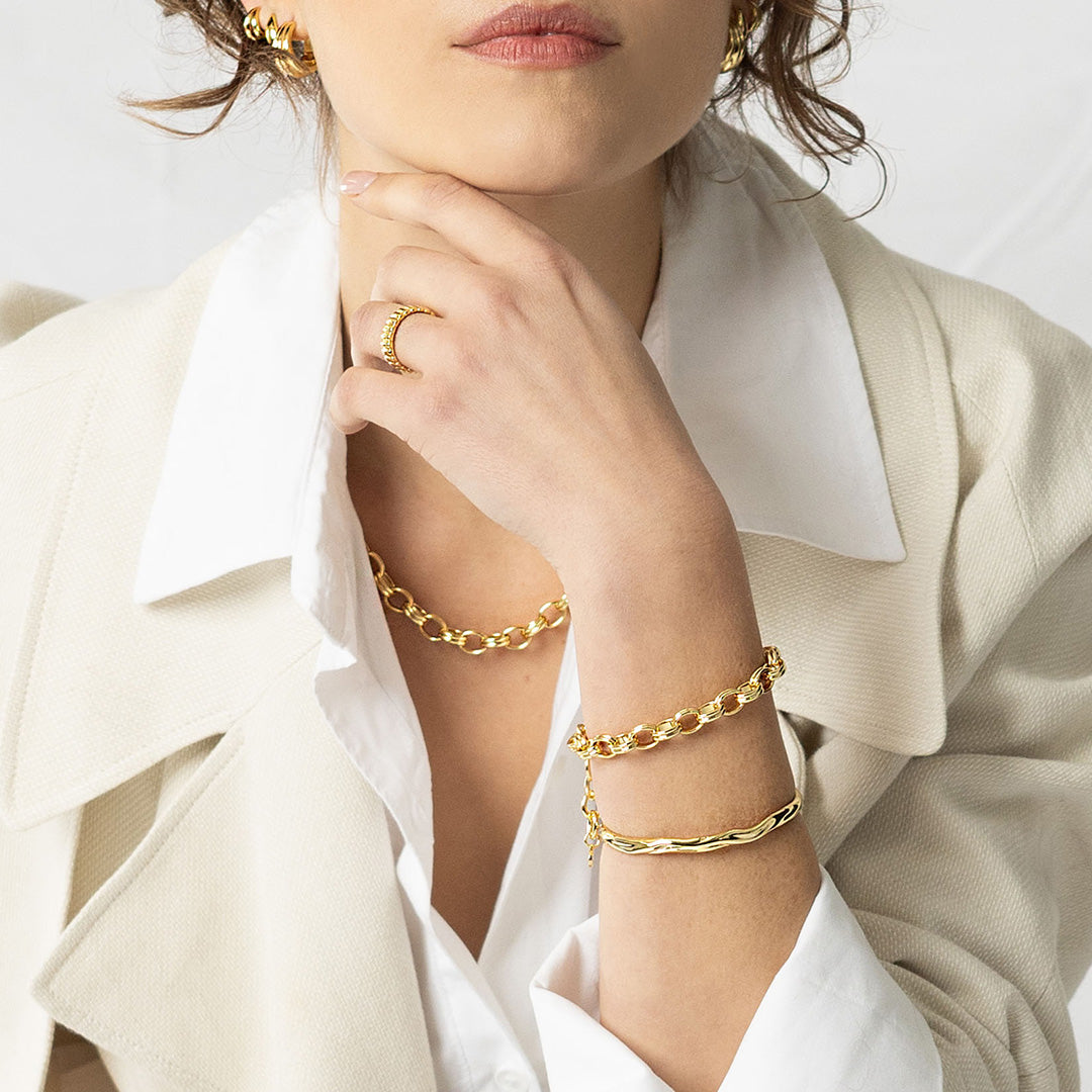 Person wearing gold bracelets and a ring on a white background