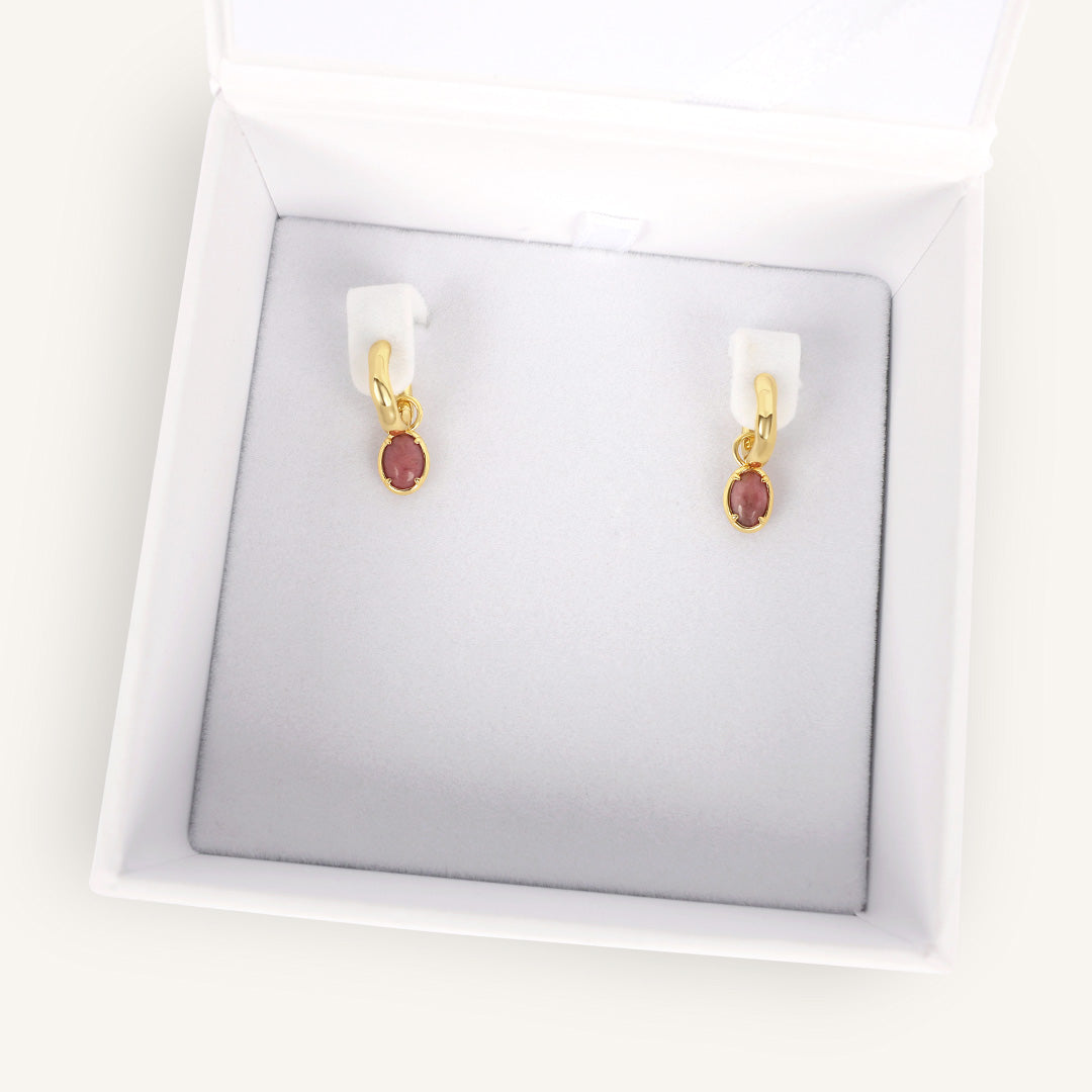 Gold earrings with red gemstones in a white box