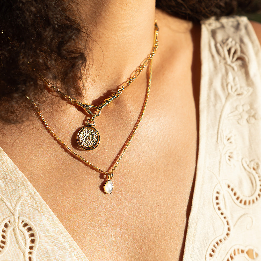 Close-up of a person wearing a gold necklace with a pendant on a blurred background