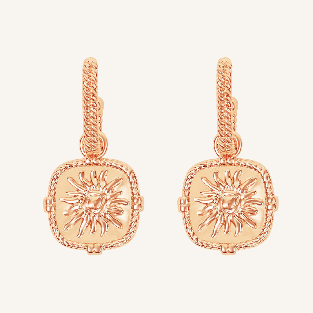 Rose gold earrings with sun design on a light pink background