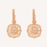 Rose gold earrings with sun design on a light pink background