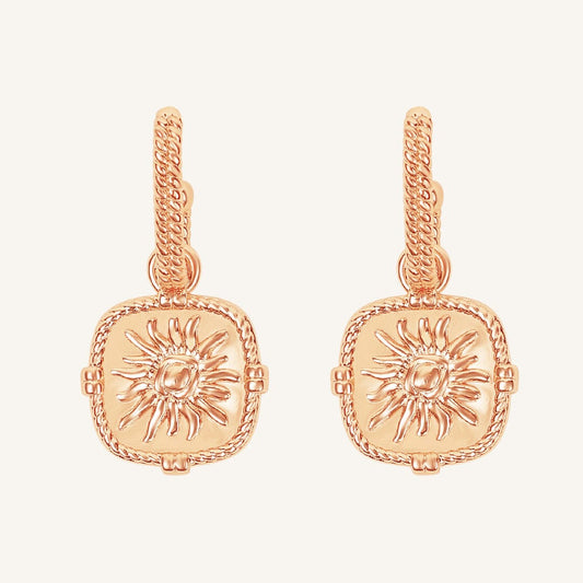 Rose gold earrings with sun design on a light pink background