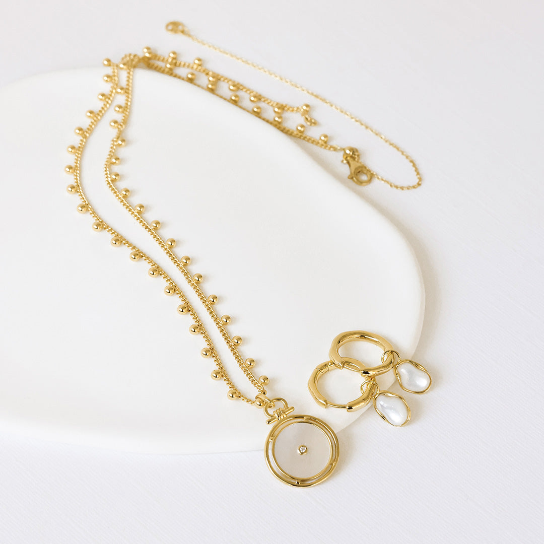 Gold necklace with a pendant and round-shaped charm on a white background