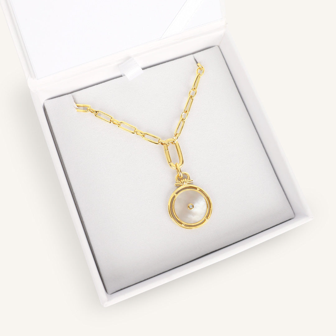 Gold necklace with a round pendant in a white box on a white background