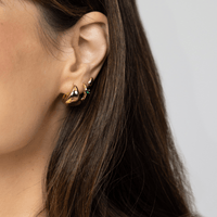 A pair of gold-colored huggie hoop earrings on a white background.