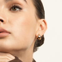 A pair of gold-colored huggie hoop earrings on a white background.