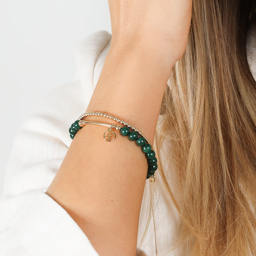 A beaded malachite charm bracelet with green stones and a gold-tone charm, worn on wrist
