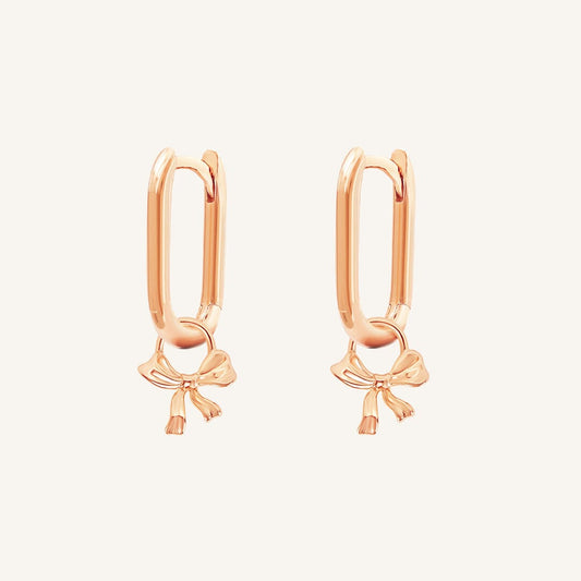 A pair of gold-tone charm hoop earrings with a simple bow design.