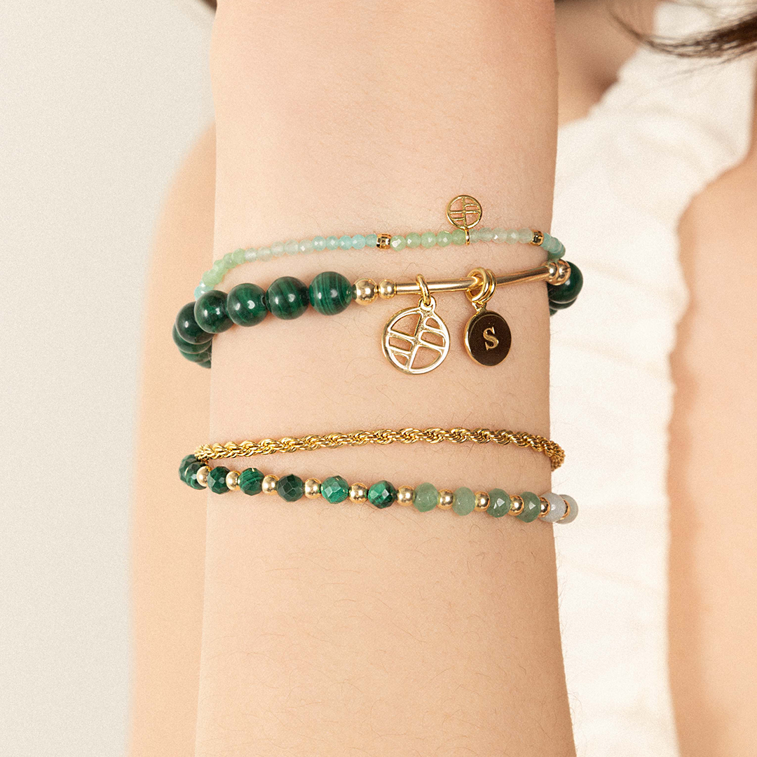 A beaded malachite charm bracelet with green stones and a gold-tone charm, worn on wrist