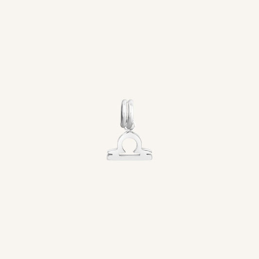 A silver charm in the shape of the Libra zodiac symbol.