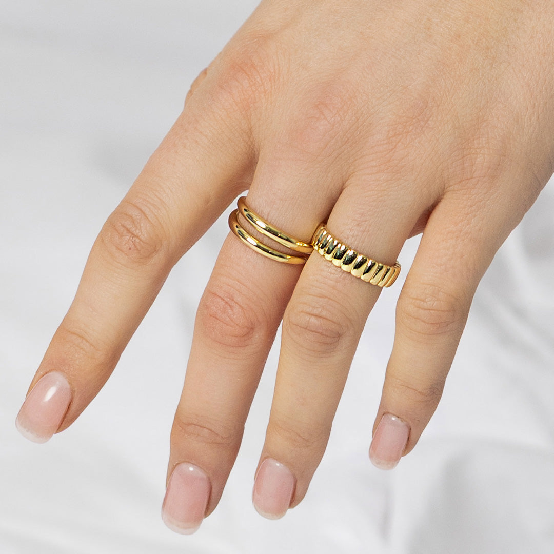 Hand wearing two gold rings on a light background