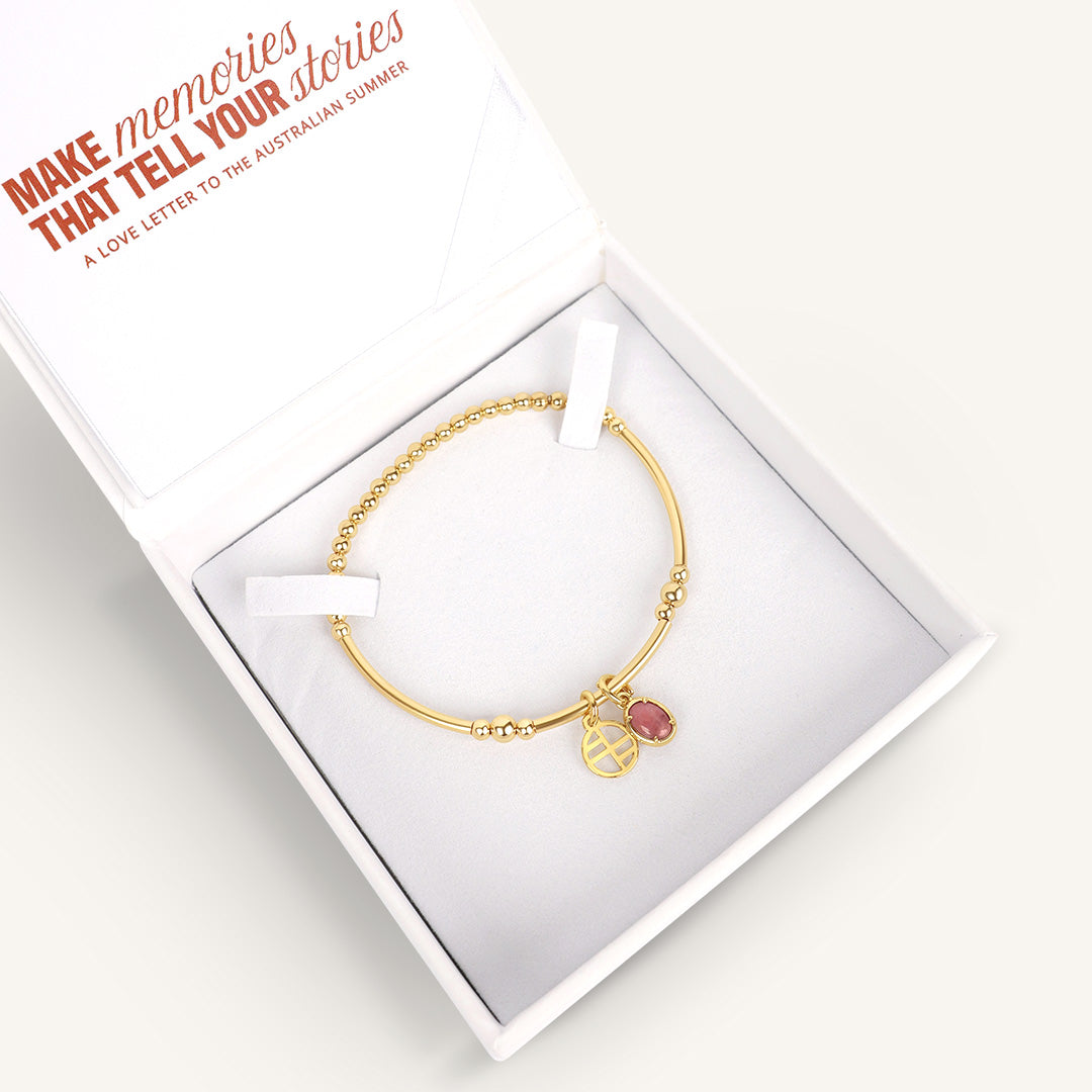 Gold bracelet with a pink gemstone in a white box, with text 'Make memories that tell your stories' on a white background.