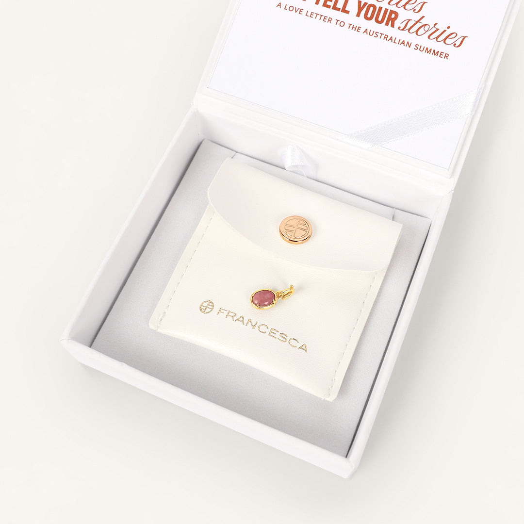 Gold jewelry with a gemstone in a branded box on a white background