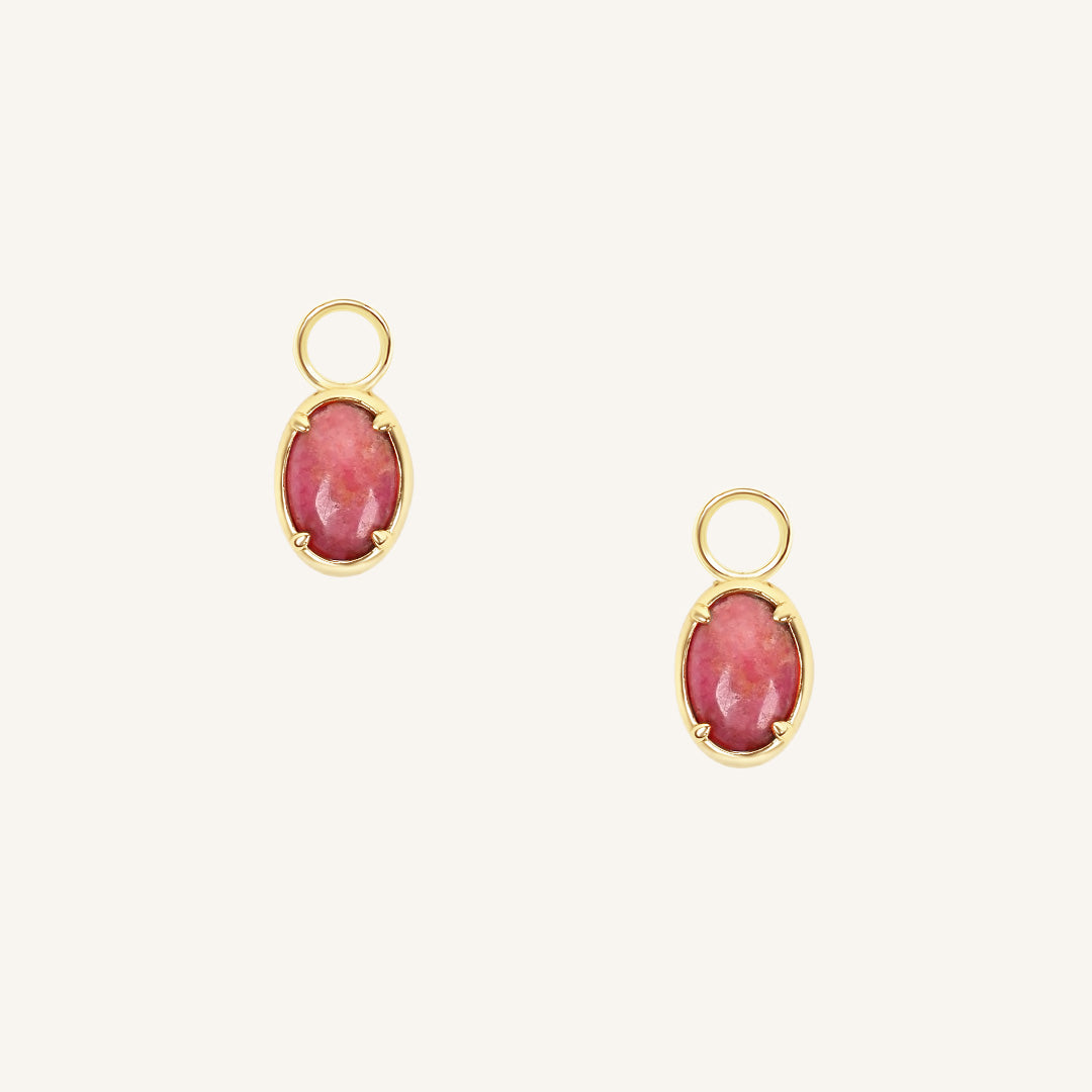 Gold hoop charms with pink gemstones on a white background