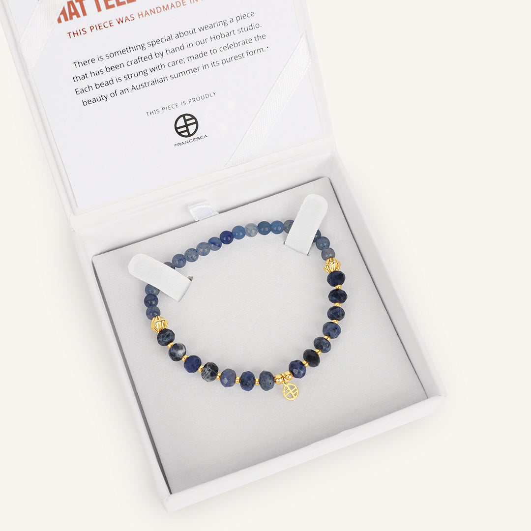 Beaded bracelet with gold accents in a white box with a card on a white background