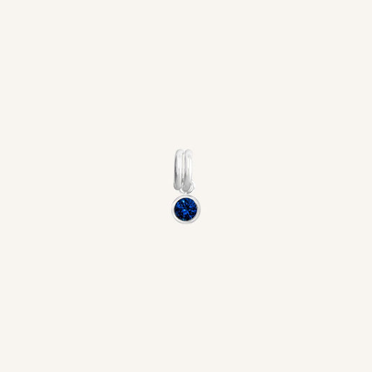 A round September birthstone charm with a blue cubic zirconia, set in silver.