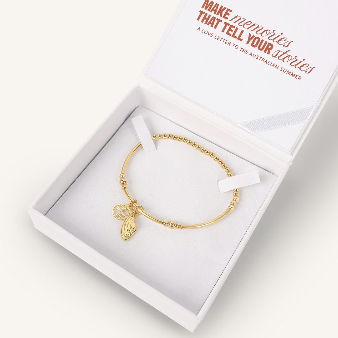 Gold bracelet with a charm in a white box, featuring text on the box.