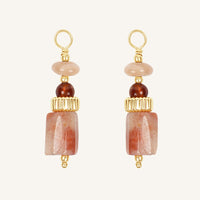 Pair of hoop charms with pink hue stones and gold accents on a white background