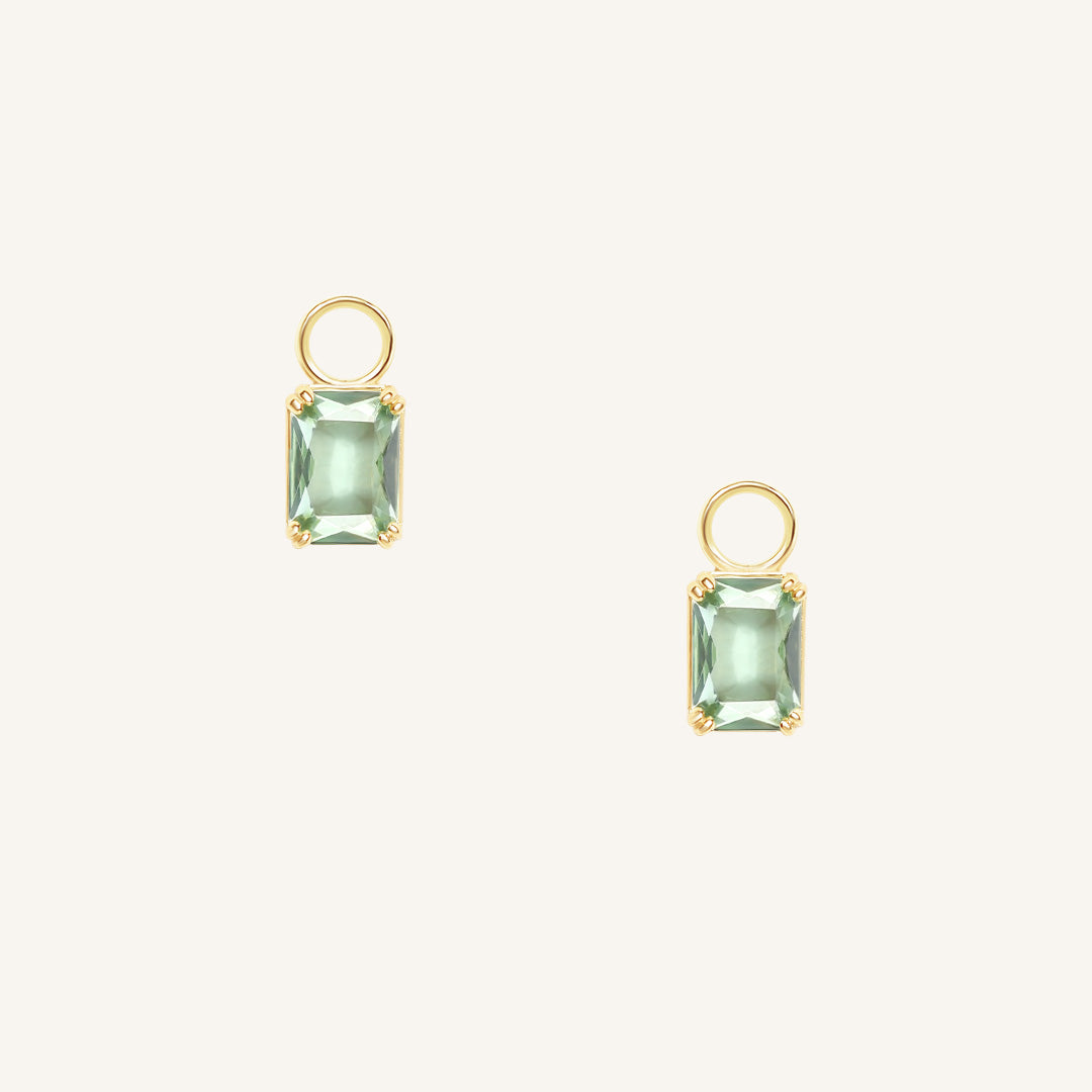 Gold hoop charms with green gemstones on a white background
