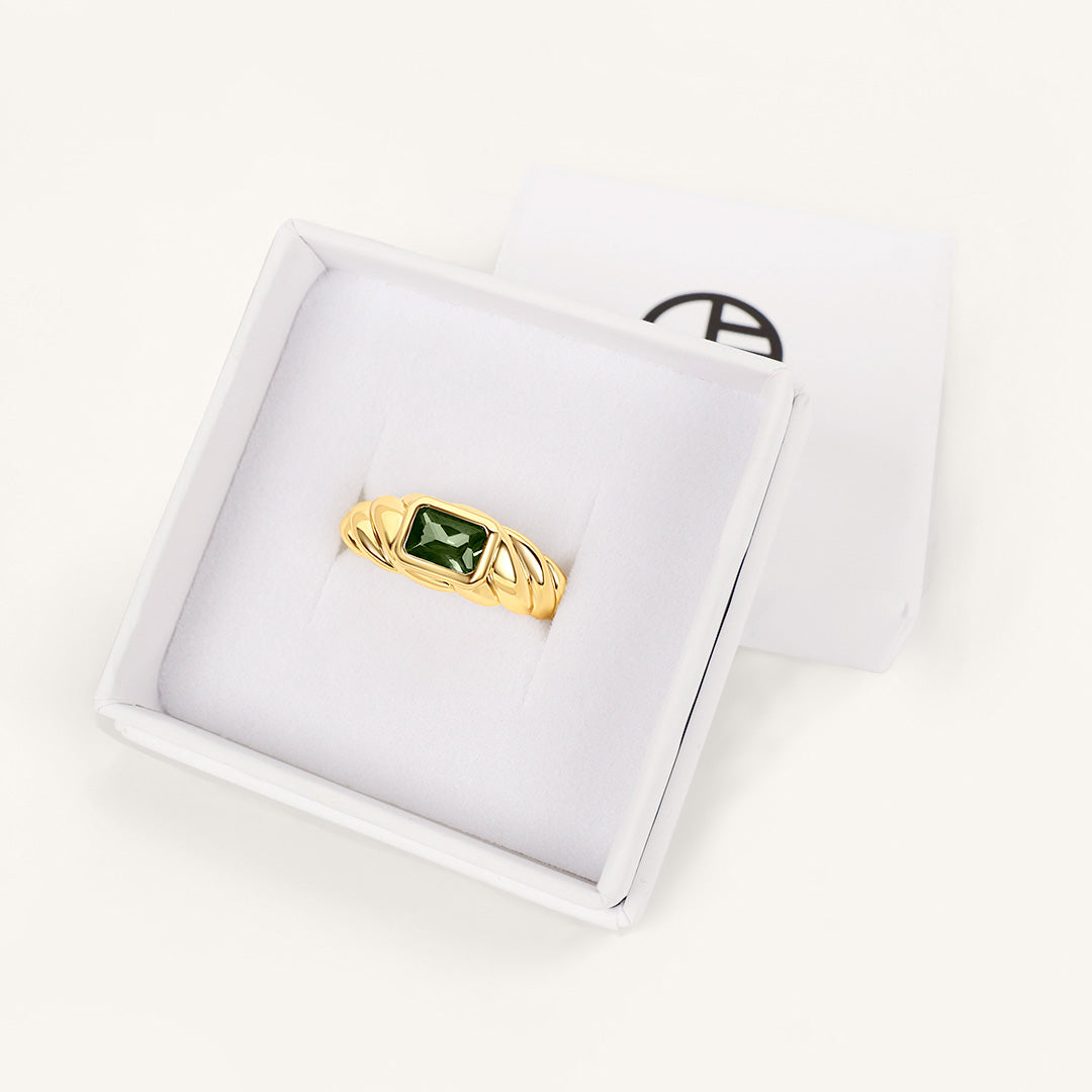 Gold ring with a green gemstone on a white display box