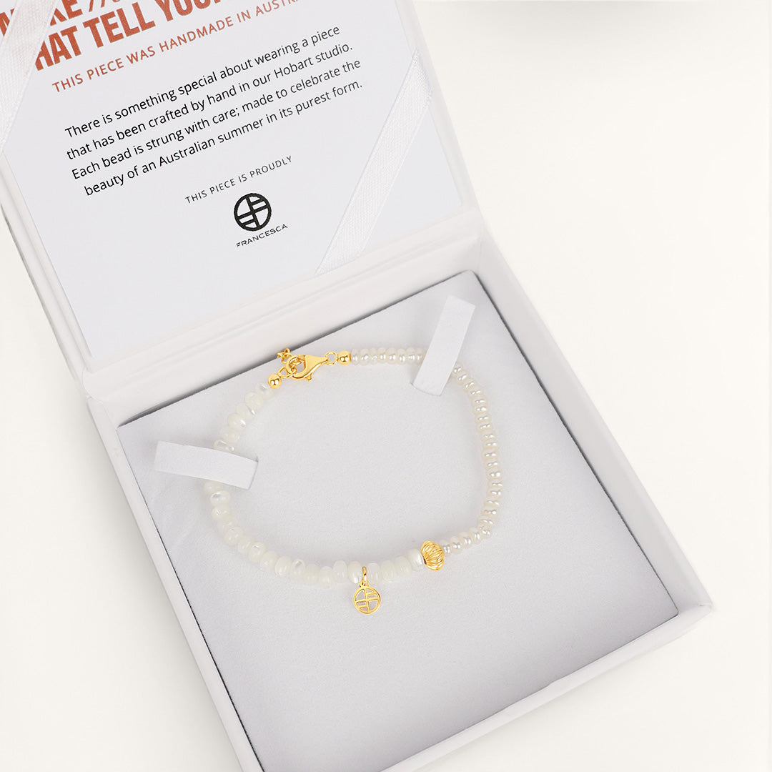 Gold bracelet with charms in a white box with a card on a light gray background