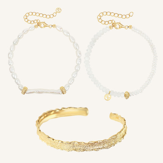 Gold bracelet and two pearl beaded bracelets on a light gray background