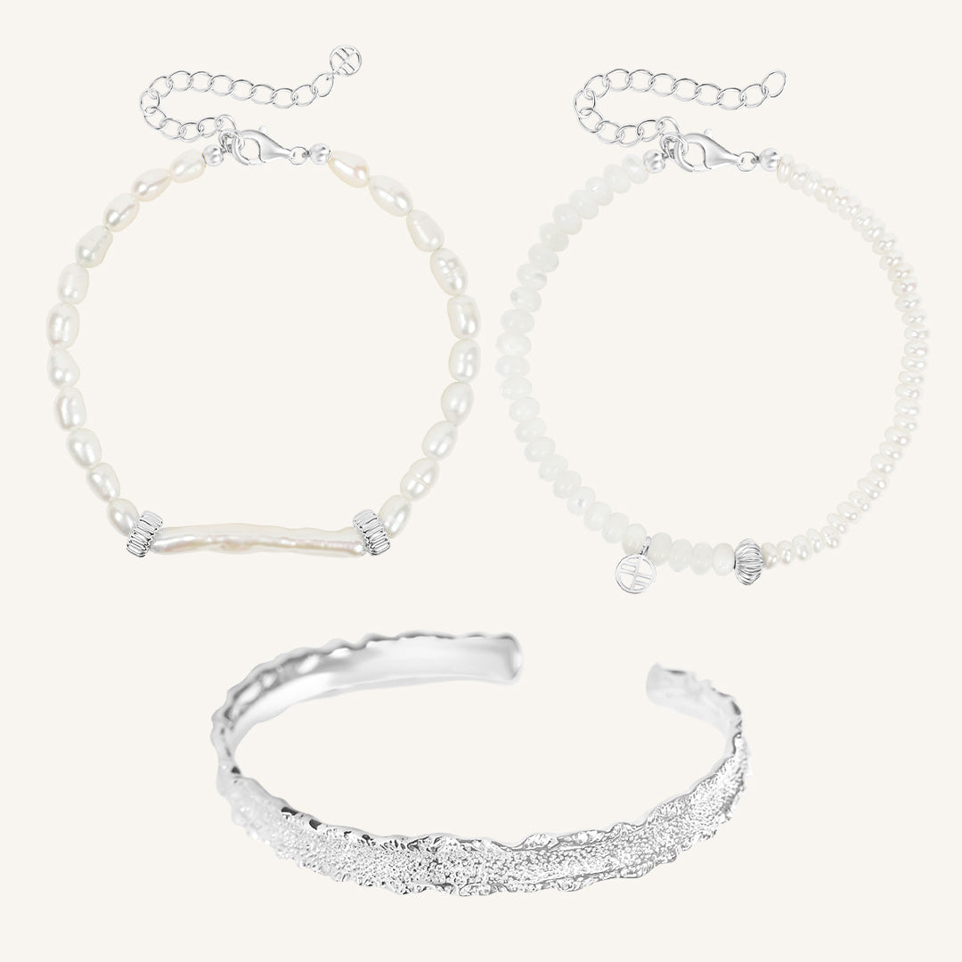 Silver bracelet and two pearl beaded bracelets on a light gray background