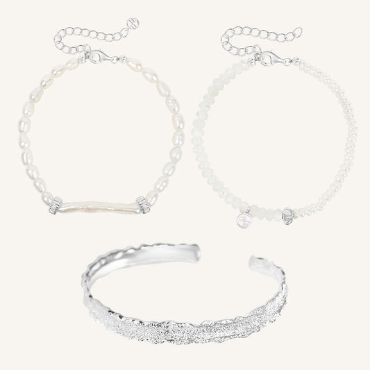 Silver bracelet and two pearl beaded bracelets on a light gray background