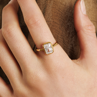 A gold-coloured ring with a white cubic zirconia, bezel set in a rectangular frame with a smooth, polished band.