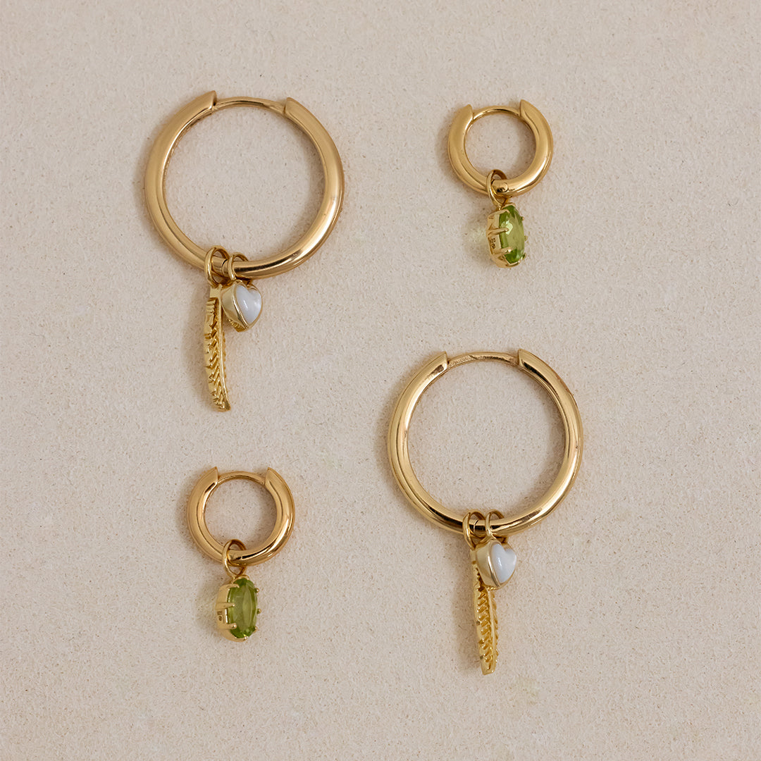 A pair of silver-tone hoop earrings with olive green charms attached to them.