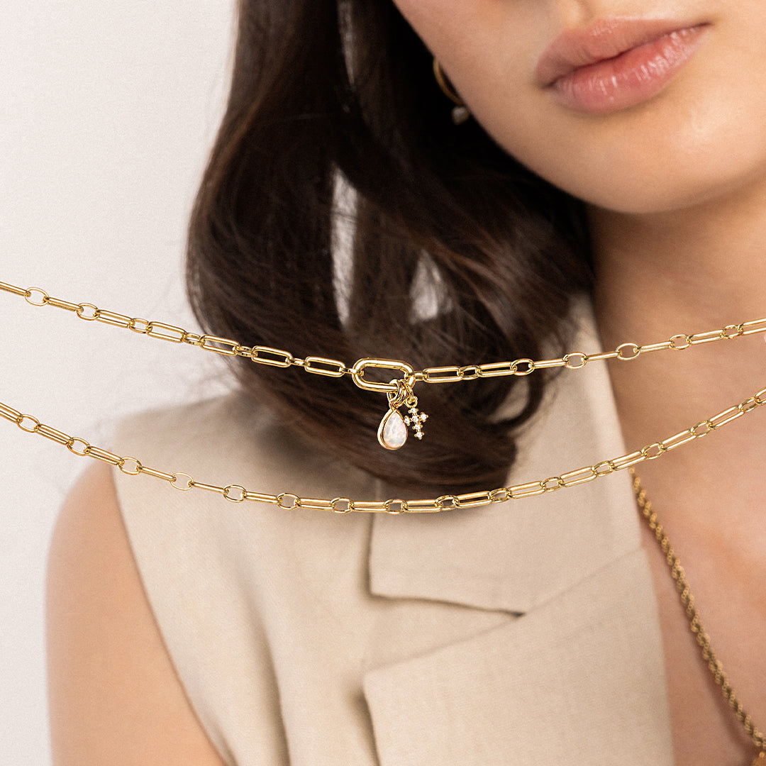 A petite gold cross charm with cubic zirconia on link chain, with another charm, held by model