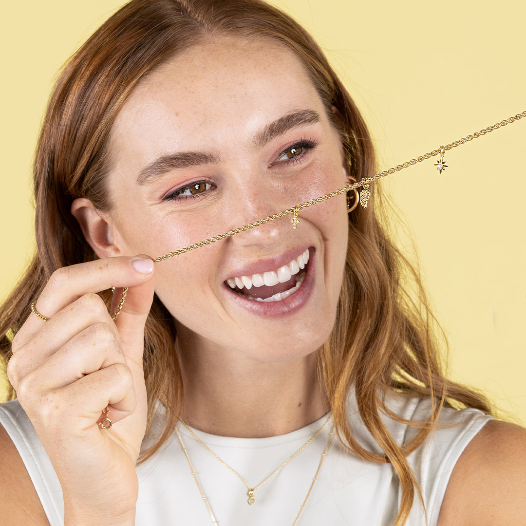 A gold-coloured angel wing charm with intricate details, attached to chain, held by model
