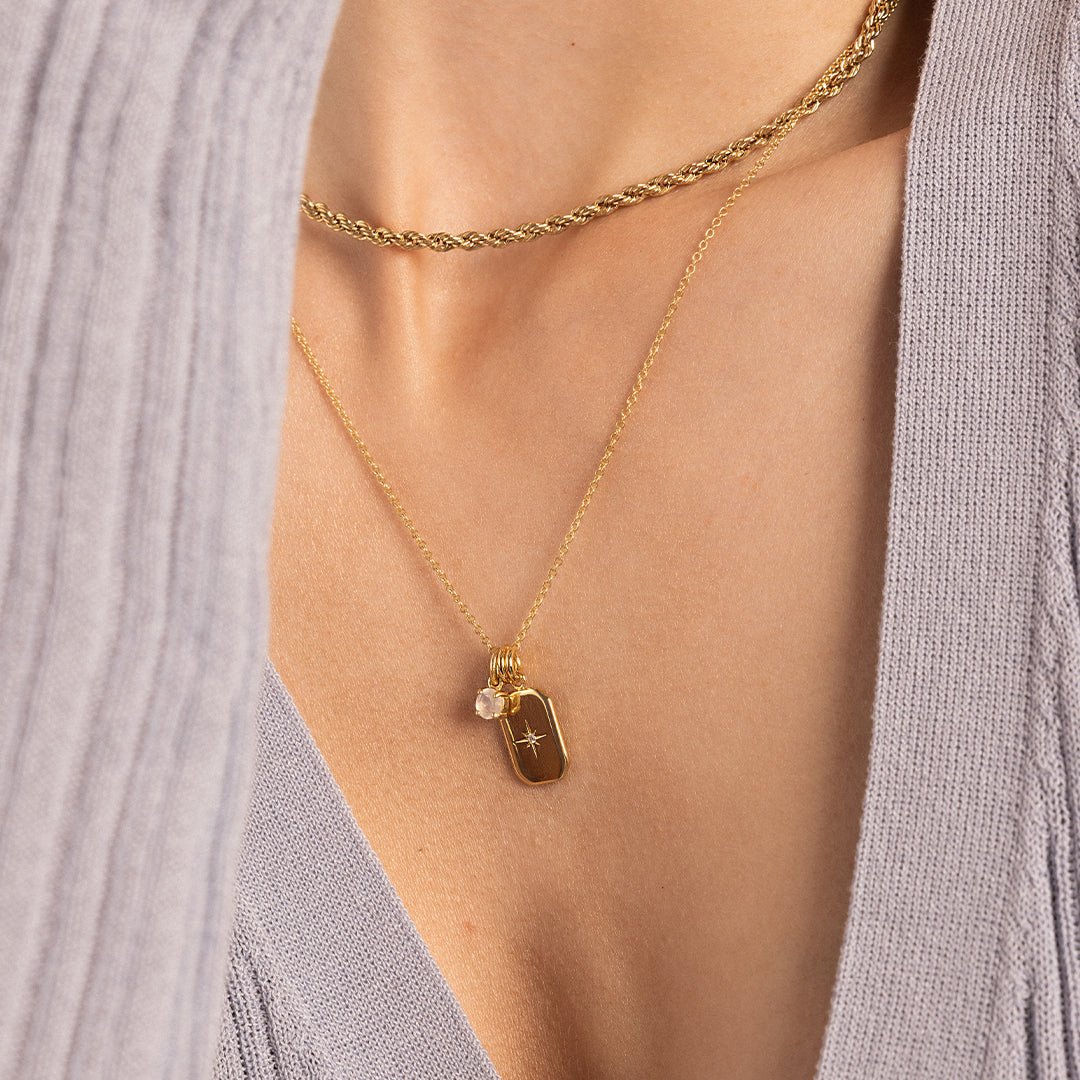 A small gold charm with a moonstone, on gold chain next to another charm, worn on neck