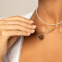 A gold heart-shaped necklace with a chain, featuring an engraved monogram initials and a date on the front.