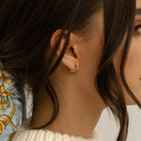 A pair of gold-colored huggie hoop earrings on a white background.